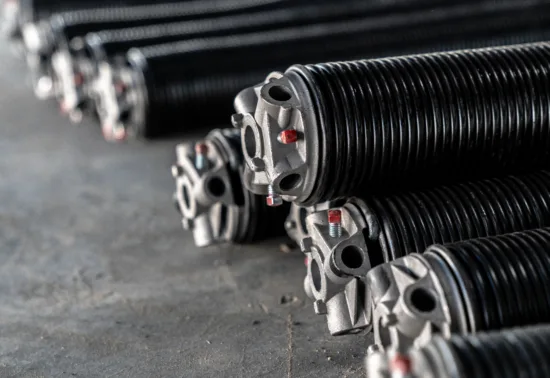 A close-up view of several black metal torsion springs with silver end fittings, arranged on a concrete floor—essential components for Illinois garage door installation.