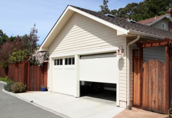 A light beige detached garage with a partially open white door, wooden fence, and driveway under a clear sky. A vehicle is partially visible inside—perfect for showcasing Illinois garage door repair expertise.