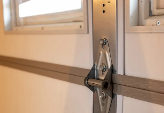 4 Signs Your Garage Door Springs Are About to Fail AdobeStock 329976241 Close-up of a metal hinge attached to a white garage door, with part of a window visible at the top—perfect for showcasing Illinois garage door installation quality and craftsmanship.