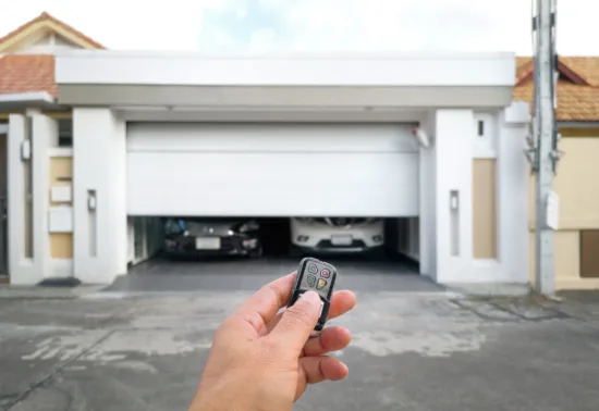 Should You DIY Garage Door Repairs? AdobeStock 246527503 A person holds a remote to open a white garage door, revealing two cars parked inside—a scene that showcases the convenience of professional Illinois garage door installation.