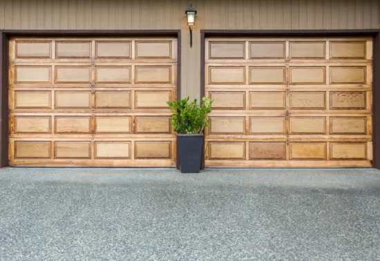 Unlock Smart Control: Connect MyQ to Alexa AdobeStock 71202825 Two wooden garage doors with a potted green plant centered between them on a concrete driveway—perfect for showcasing expert Illinois garage door repair or installation services.