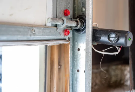 4 Signs Your Garage Door Springs Are About to Fail AdobeStock 342122892 Close-up of a garage door sensor with visible wiring and a green indicator light, mounted on a metal frame near the door track—ideal for those seeking reliable Wisconsin garage door repair.