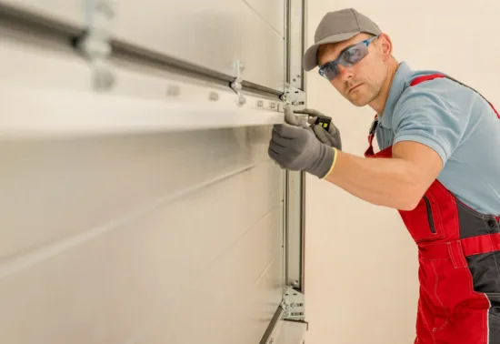A worker wearing safety glasses and gloves installs or repairs a garage door in Wisconsin, using a tool to adjust the metal track as part of professional Wisconsin garage door repair.