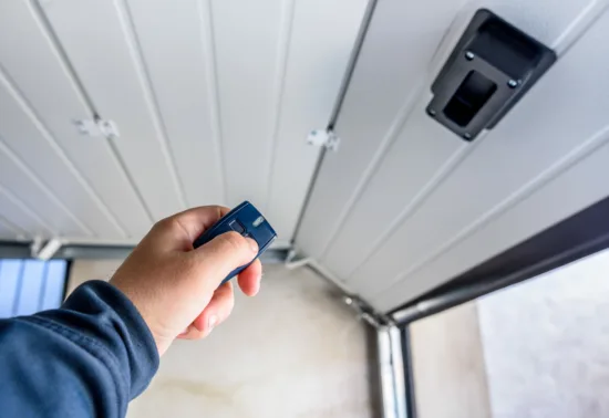 A person holds a remote control, aiming it at the ceiling-mounted mechanism of a partially open garage door, perfect for showcasing Illinois garage door installation.
