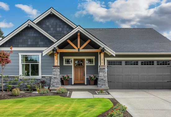 Modern suburban house with gray siding, gabled roof, wooden accents, front porch, landscaped yard, and a two-car garage—ideal for those seeking reliable Illinois garage door repair under a partly cloudy sky.