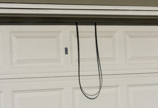 A detached garage door opener chain hangs down in front of a closed white garage door, suggesting a garage door opener repair may be needed in Conover.