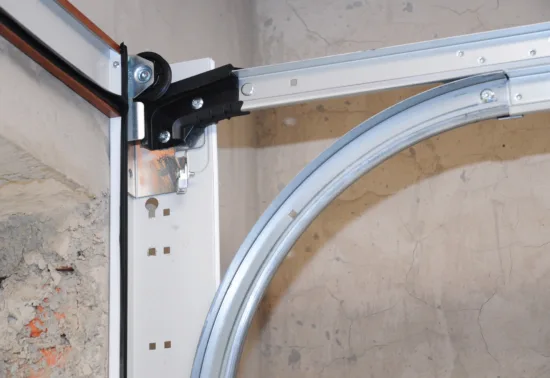 Close-up of a metal garage door track and roller system on a cracked concrete wall, highlighting the need for garage door track replacement in Eagle River.