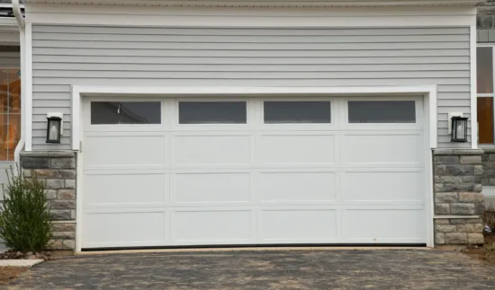 A closed white garage door with four rectangular windows at the top, set in a house with gray siding and stone accents. Two black lantern lights are mounted on either side, showcasing the importance of regular garage door maintenance in South Elgin to keep everything looking pristine and functioning smoothly.